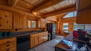 Cozinha de cabana rústica com armários de madeira, lava-louças, geladeira e fogão.