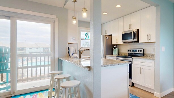 A modern kitchen with white cabinets, a stainless steel refrigerator, a microwave, and a stove. There are three white bar stools near the kitchen counter. - 2nd Floor, Shared Pool and Hot Tub, Golf Cart Access (Port Aransas)