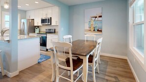 A modern kitchen with white cabinets, stainless steel appliances, and a dining area with a wooden table and white chairs. - 2nd Floor, Shared Pool and Hot Tub, Golf Cart Access (Port Aransas)