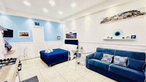 Een moderne hotelkamer met een blauwe bank, een bed met een blauw dekbed en een klein rond tafeltje, en een tv aan de muur.