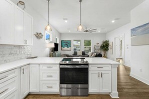 Une cuisine moderne avec des meubles blancs, un four en acier inoxydable, des luminaires suspendus et un ventilateur de plafond.