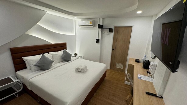 Een hotelkamer met een bed, een bureau met stoel, een televisie en een airconditioning.