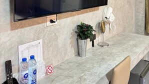 Een televisie die aan een muur is bevestigd, met het Netflix-logo, een kleine potplant, een haardroger en een afstandsbediening op een marmeren aanrecht.