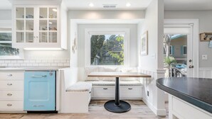 A kitchen with a built-in bench, white cabinetry, and a blue dishwasher. - Lazy Bear Beach House (Capitola)