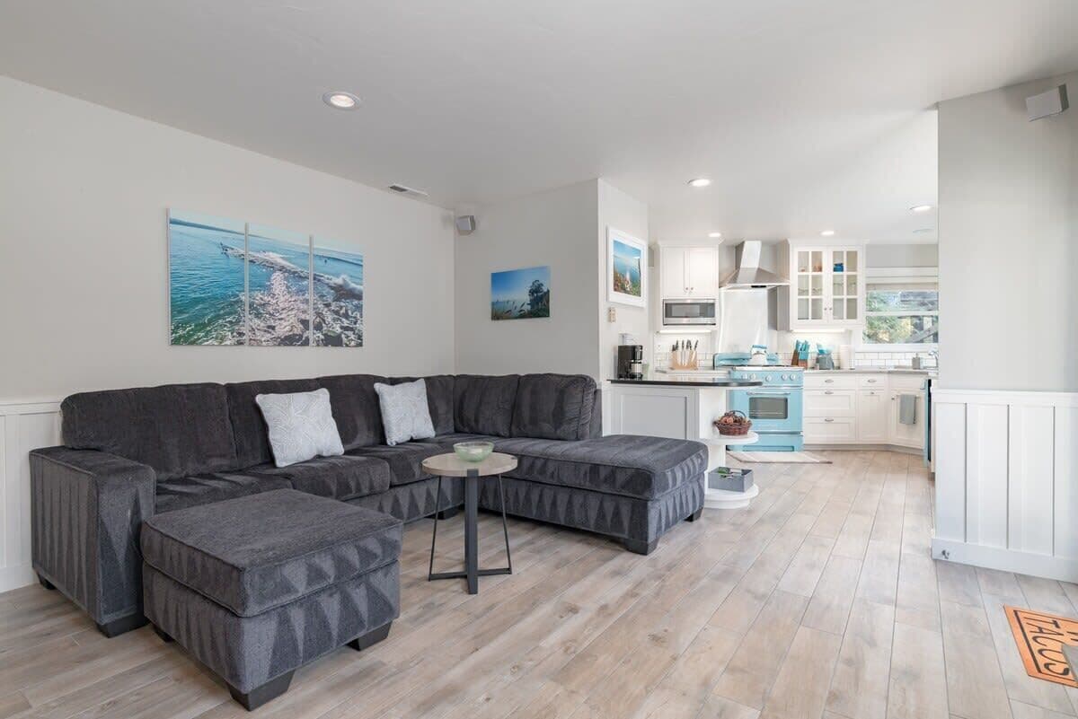 A modern living room with a sectional sofa, a small round table, and a kitchen in the background.