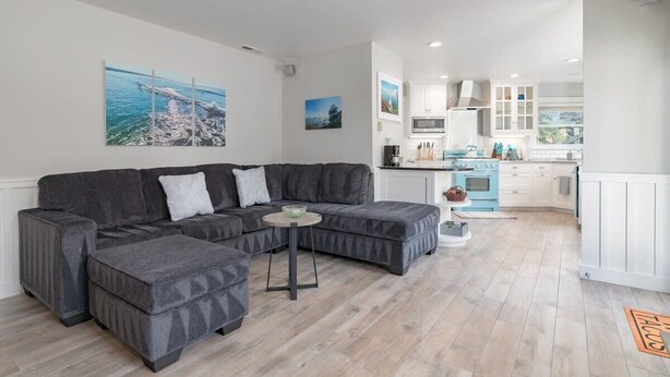 A modern living room with a sectional sofa, a small round table, and a kitchen in the background. - Lazy Bear Beach House (Capitola)