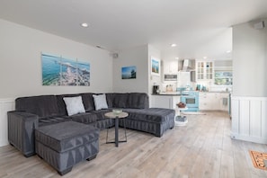 Ein modernes Wohnzimmer mit einem Ecksofa, einem kleinen runden Tisch und einer Küche im Hintergrund.