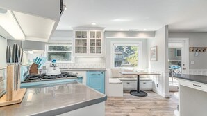 A modern kitchen with a central island, white cabinetry, and a window overlooking a residential area. - Lazy Bear Beach House (Capitola)