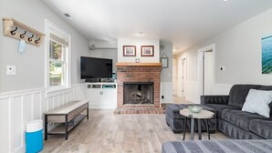 A living room with a fireplace, a sofa, a TV, and a bench. - Lazy Bear Beach House (Capitola)
