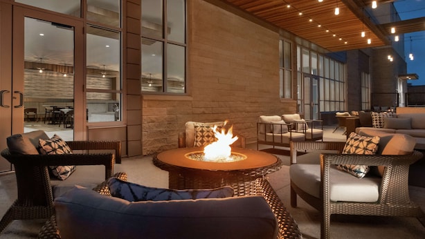 An outdoor seating area with wicker furniture, a central fire feature, and large windows. - Hilton Garden Inn Austin North - Near the Domain (Austin)