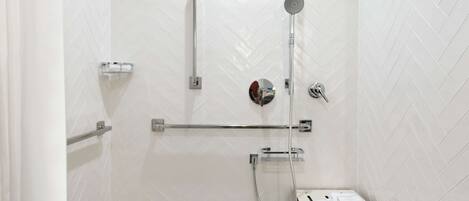 A modern bathroom with white herringbone tiles, a glass shower enclosure, a handheld showerhead, and a towel rack.
