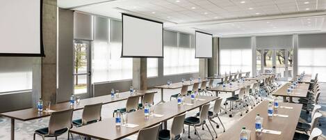 A conference room with multiple tables, chairs, and large screens.