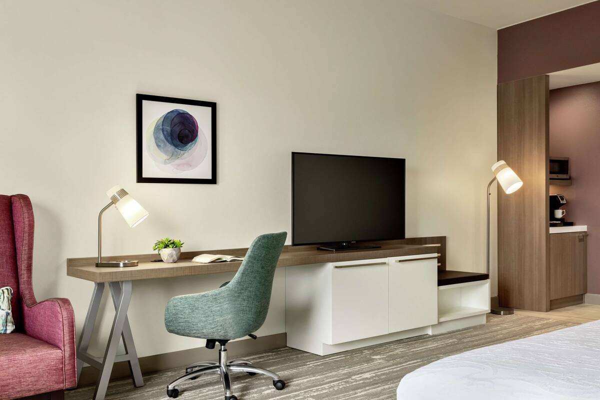 A modern hotel room with a desk, chair, television, and a bed.