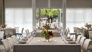 A dining area with tables set for a meal, large windows with a view of trees, and a modern interior design. - Hilton Garden Inn Austin North - Near the Domain (Austin)