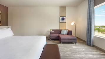 Quarto de hotel com uma cama grande, um sofá, uma mesinha com abajur e vista para o exterior.