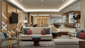 A spacious living area with a sofa set, ottomans, and a coffee table. There is a dining area with a table and chairs in the background. - Hilton Garden Inn Austin North - Near the Domain (Austin)