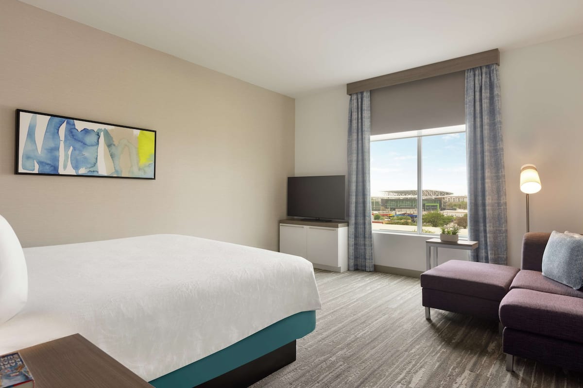 A hotel room with a bed, a TV, a sofa, and a window with a view.
