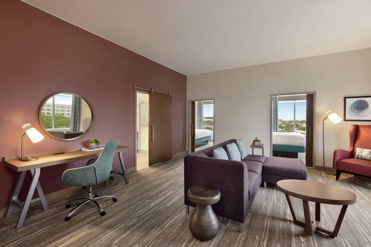 A hotel room with a desk, chair, sofa, and a small table.