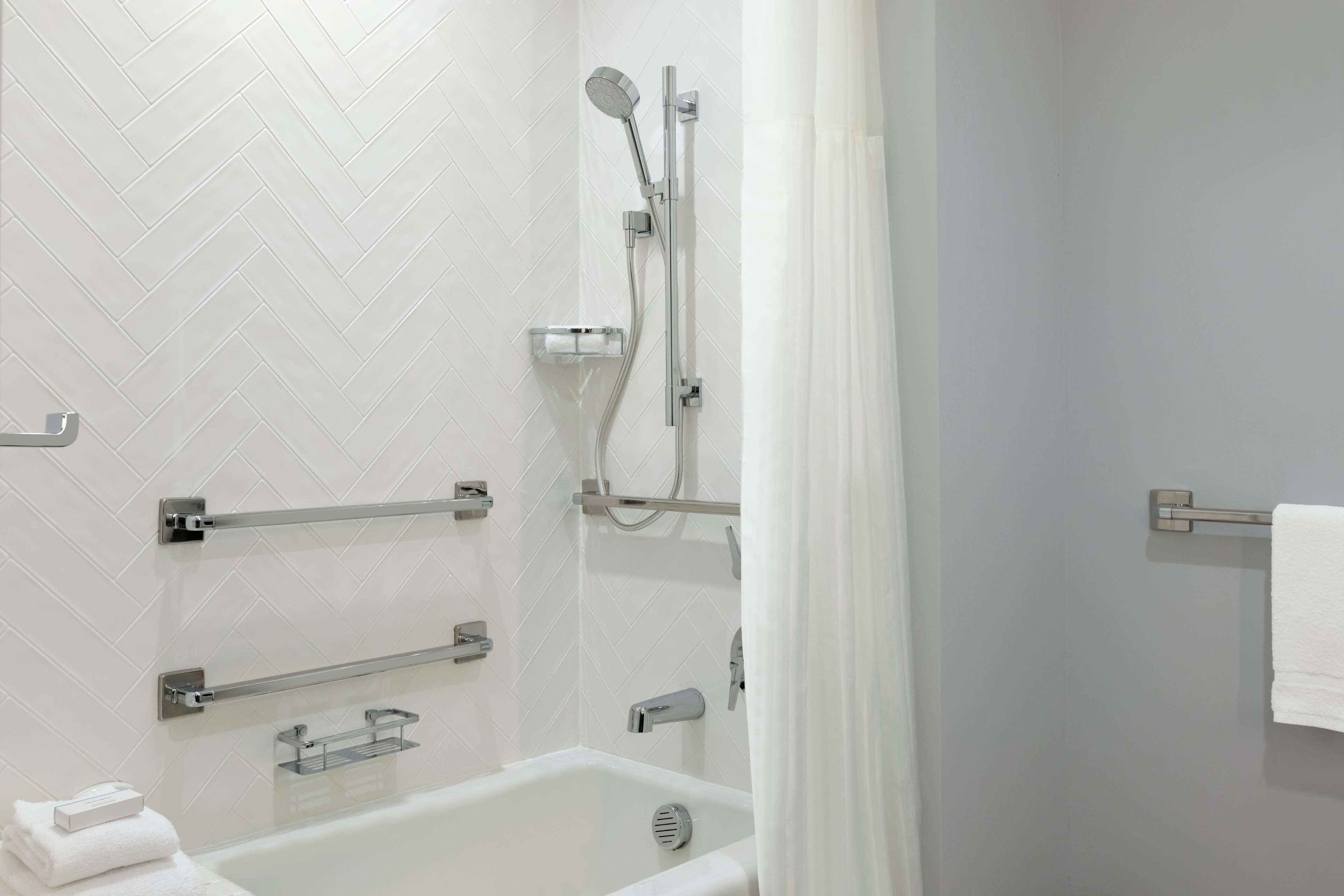A modern bathroom with a white herringbone tile wall, a freestanding bathtub, a shower with a handheld showerhead, and a towel rack.