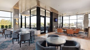 A modern hotel lobby with round tables, comfortable seating, large windows, and a view of the city.
