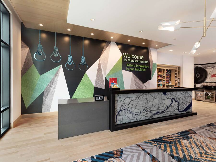 Ein moderner Hotel-Empfangsbereich mit geometrischer Wandgestaltung, einer Rezeption und einer Kaffeestation.