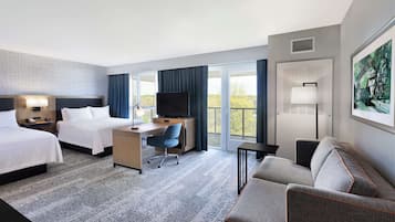 A hotel room with two beds, a desk, a chair, a sofa, and a TV.