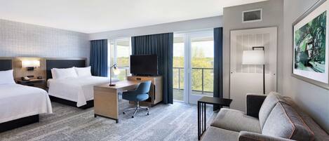 A hotel room with two beds, a desk, a chair, a sofa, and a TV.