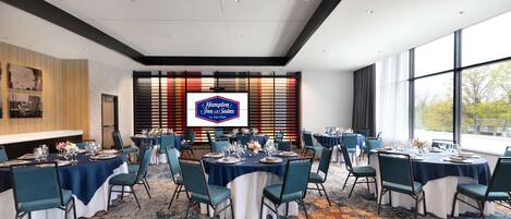 A conference room with round tables, chairs, and a large screen displaying the Hampton Inn logo.