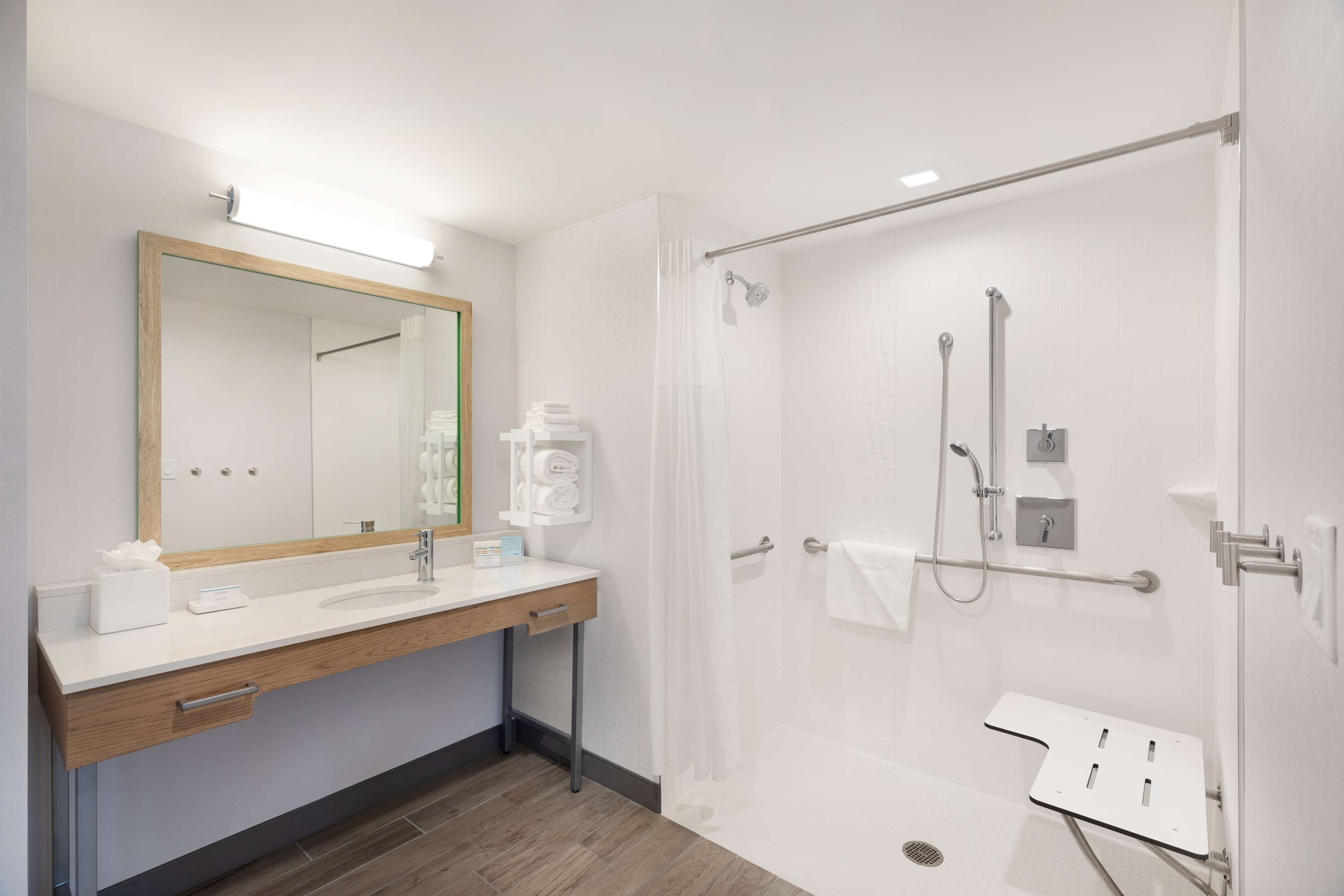 A modern bathroom with a wooden vanity, a large mirror, a shower with a glass door, and a white sink.