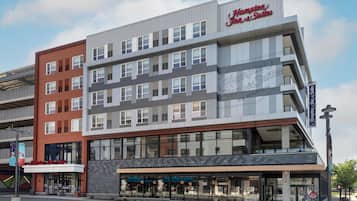 Un hotel moderno con varios pisos, grandes ventanales y un llamativo letrero de Hampton Inn & Suites.