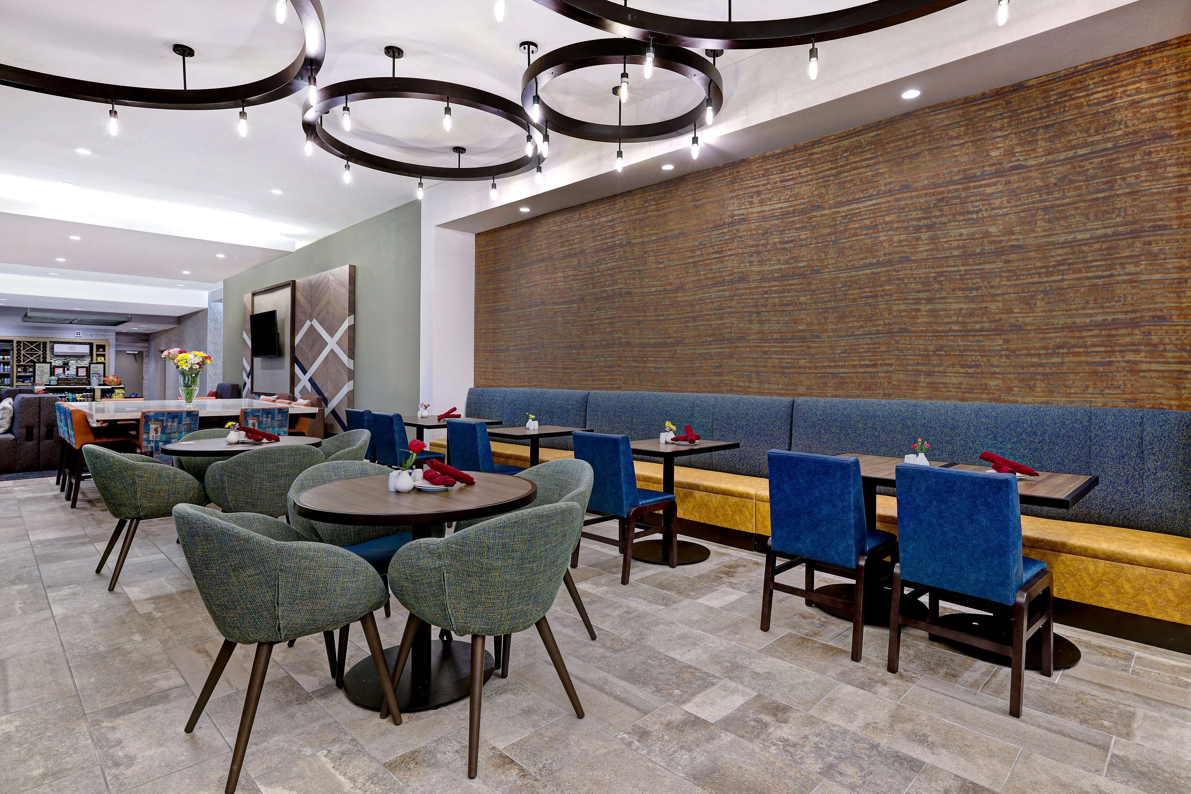 Un restaurante moderno con mesas redondas y asientos acolchados azules, que cuenta con una pared de ladrillo e iluminación contemporánea.