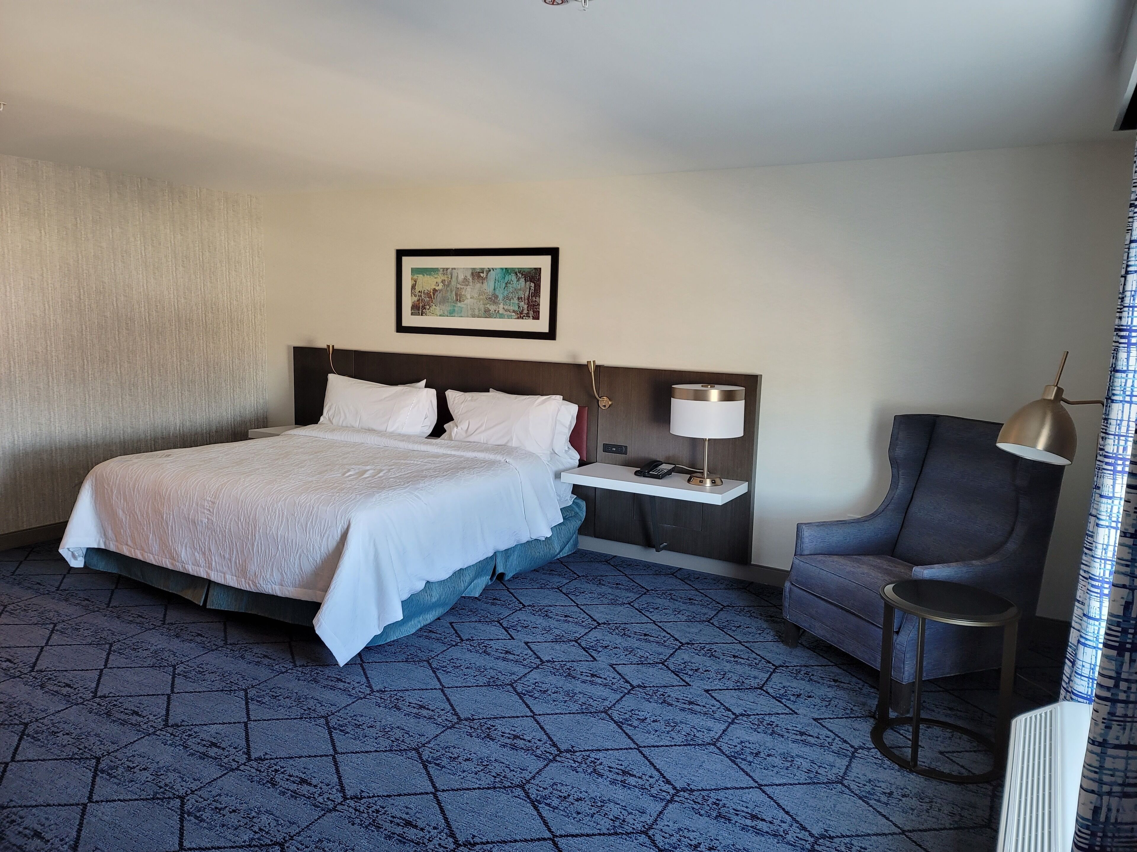 Une chambre d’hôtel avec un grand lit, une table de chevet avec une lampe, une chaise et une petite table.