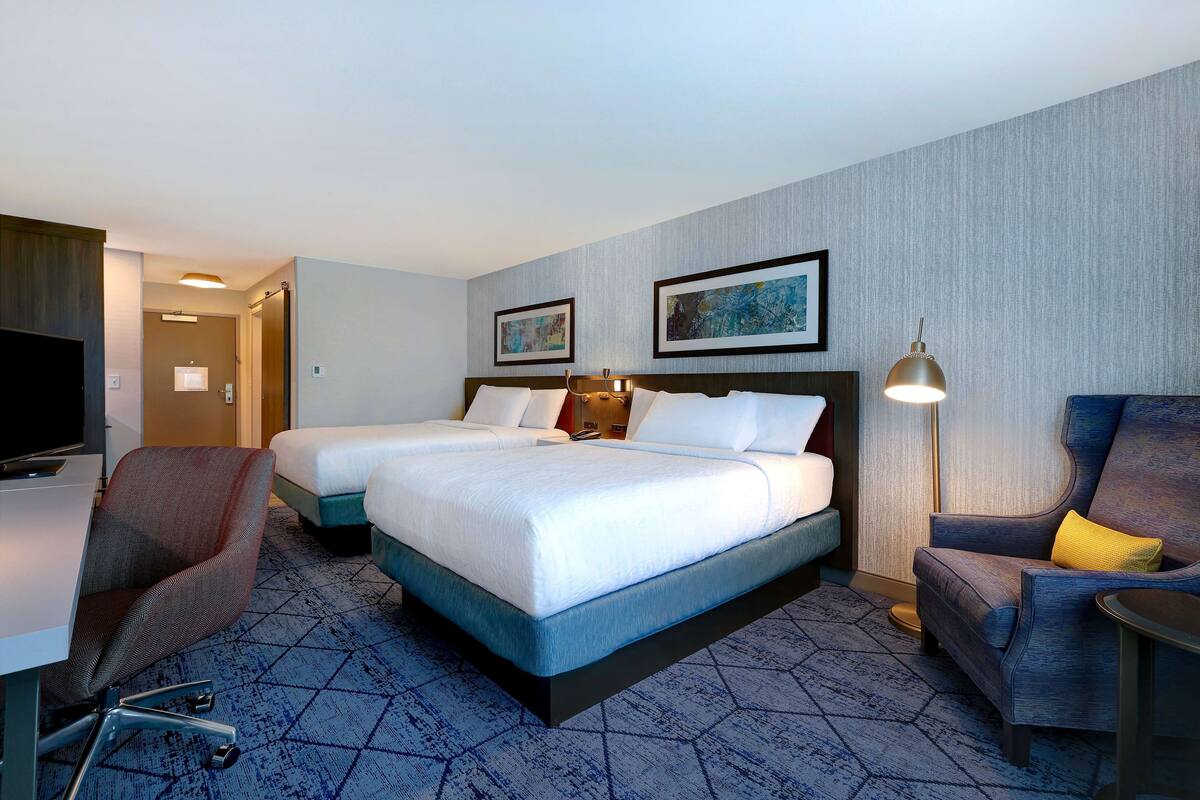 Ein Hotelzimmer mit einem großen Bett, zwei Nachttischen, einem Schreibtisch mit Stuhl und einem Fernseher.