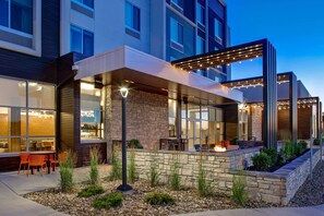 A modern hotel exterior with large windows, outdoor seating, and a stone retaining wall. - Hilton Garden Inn Cedar Rapids (Cedar Rapids)