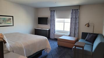 A hotel room with a bed, a desk, a chair, a TV, a window with curtains, and a floor heater.