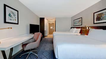 Quarto de hotel com secretária, duas camas, uma cadeira e obras de arte nas paredes.