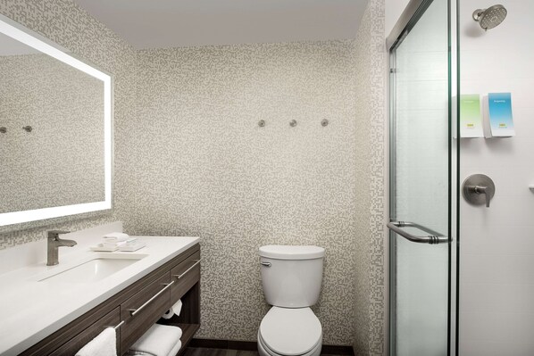 A modern bathroom with a white toilet, a glass shower enclosure, and a vanity with a mirror and sink.