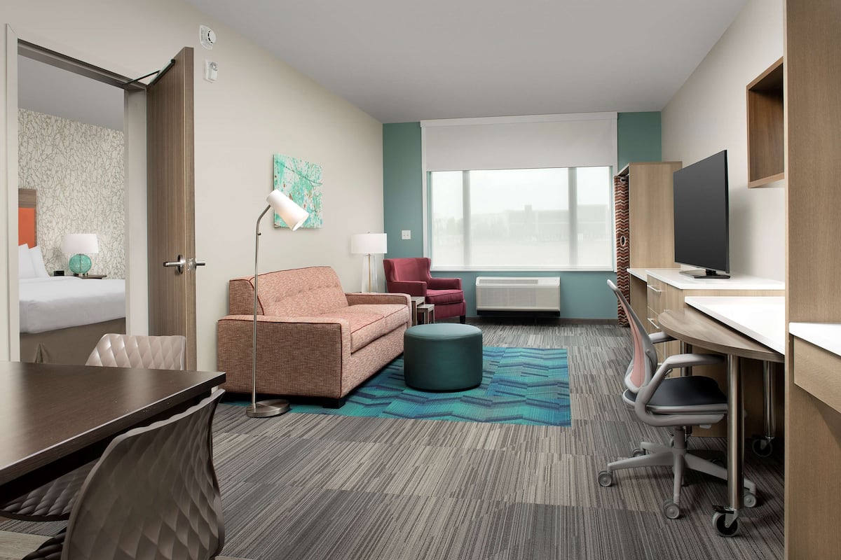 A hotel room with a bed, a desk, a chair, a sofa, a TV, and a window.