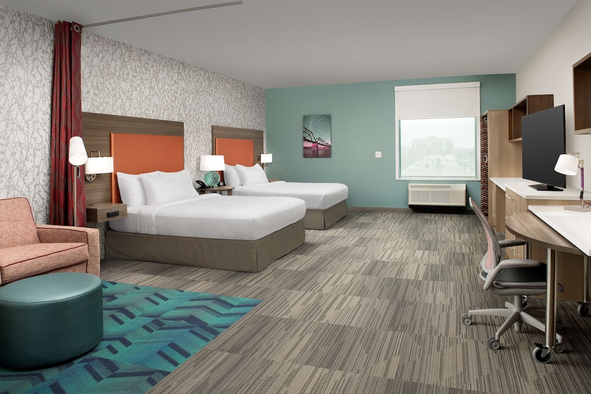 A hotel room with two beds, a desk, a chair, a couch, and a TV.