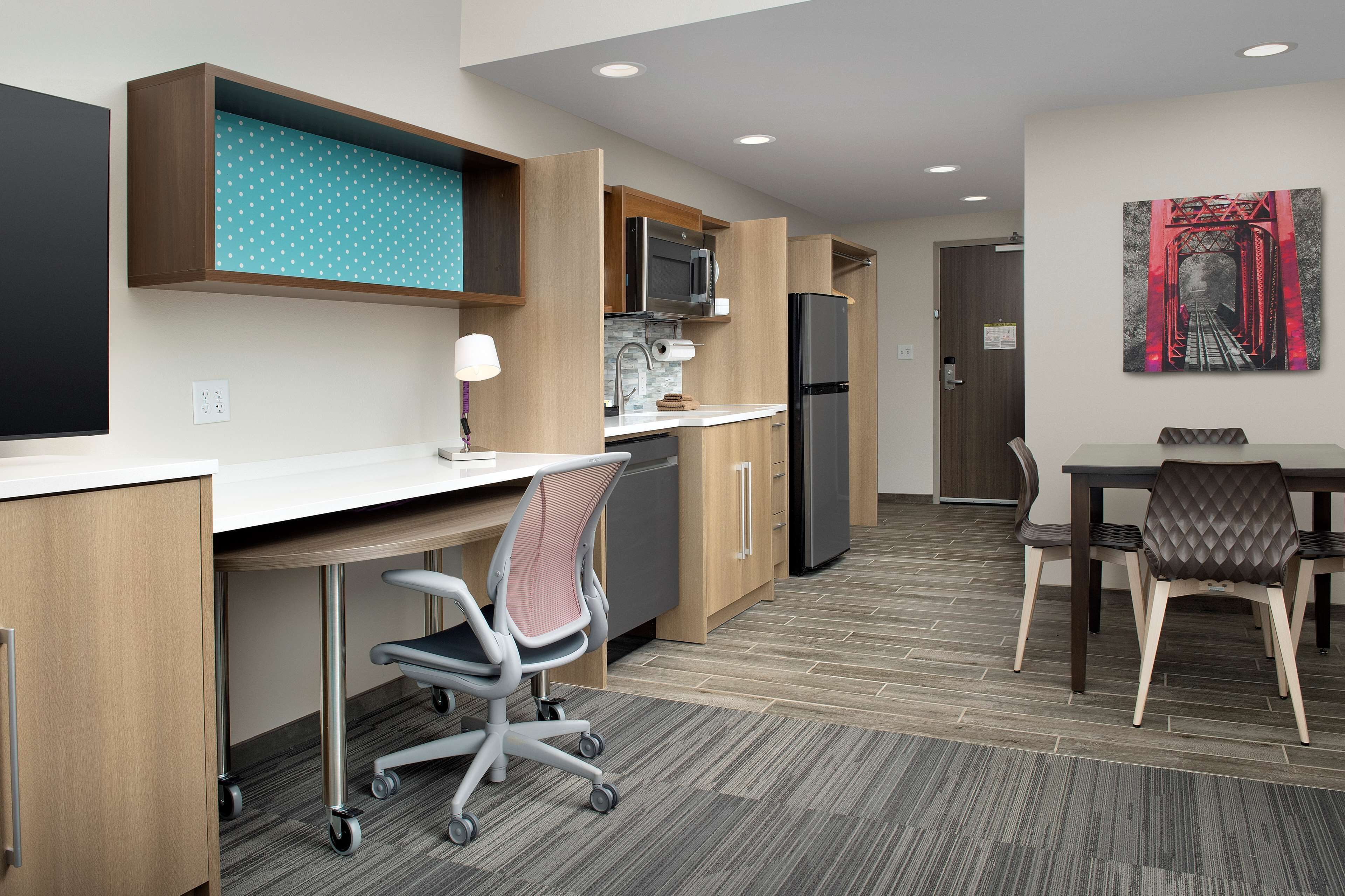 A modern kitchen with a microwave, refrigerator, and wooden cabinets. There is a dining area with a table and chairs.