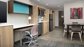 A modern kitchen with a microwave, refrigerator, and wooden cabinets. There is a dining area with a table and chairs.
