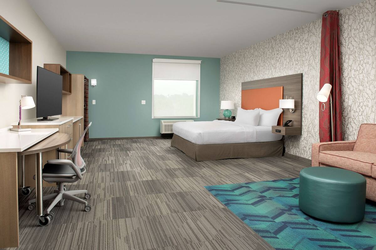 A hotel room with a bed, desk, chair, and ottoman.