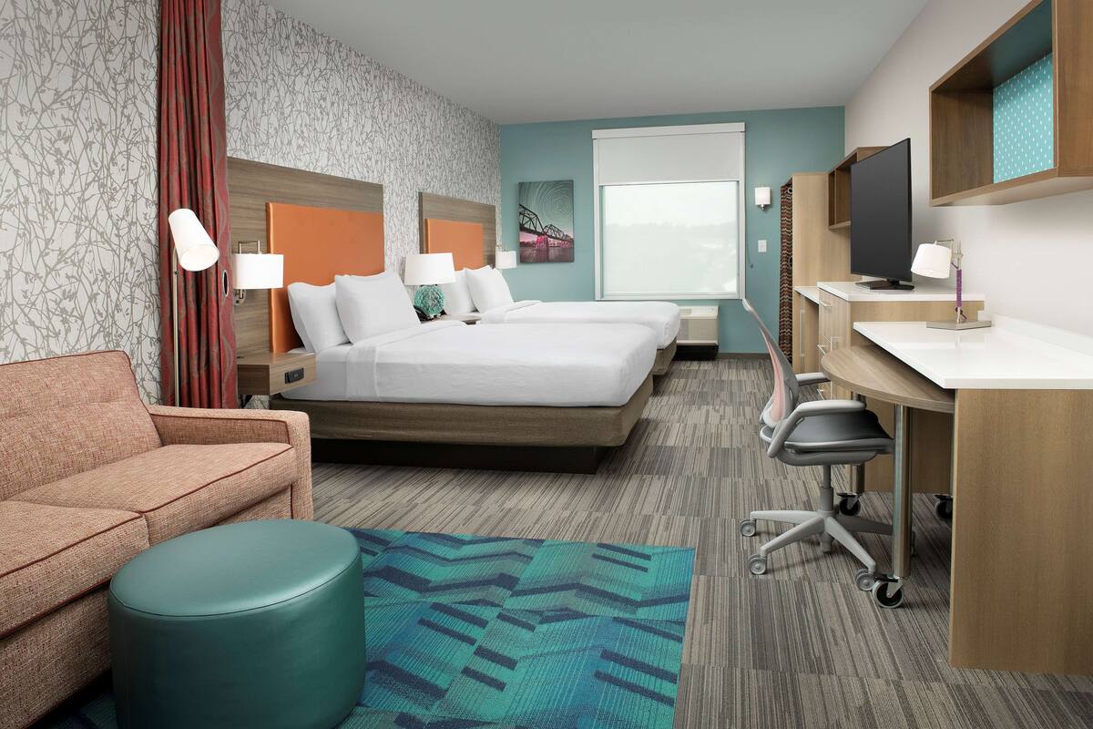 A hotel room with a bed, a desk, a chair, a sofa, and a TV.
