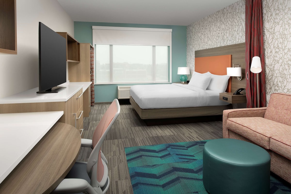 A hotel room with a bed, a desk, a television, a chair, a sofa, and a window with a view.