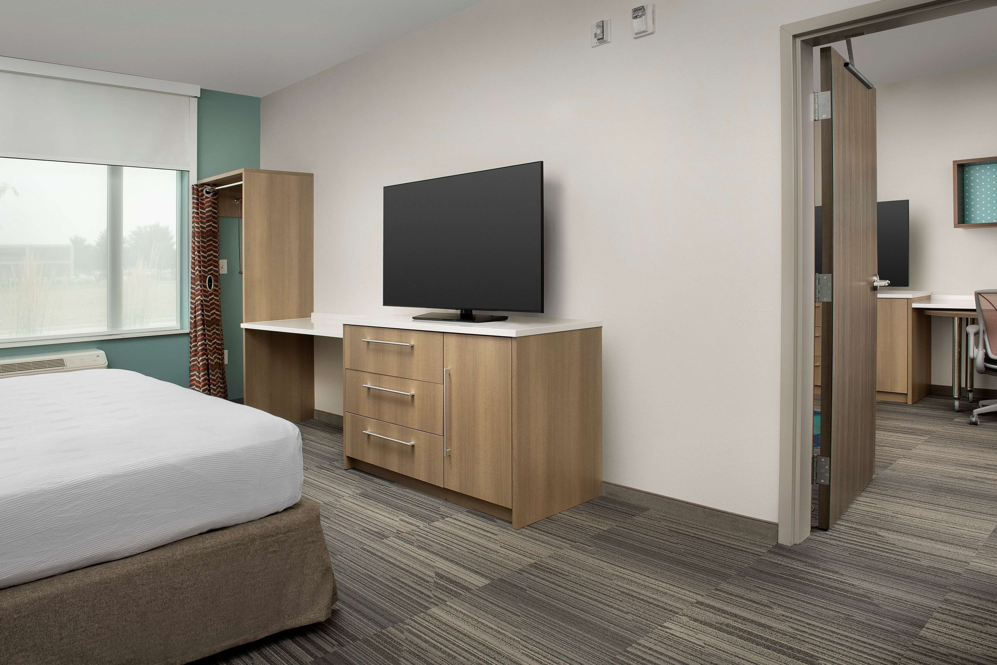 A hotel room with a bed, a TV on a wooden stand, a desk with a chair, and a bathroom visible through an open door.