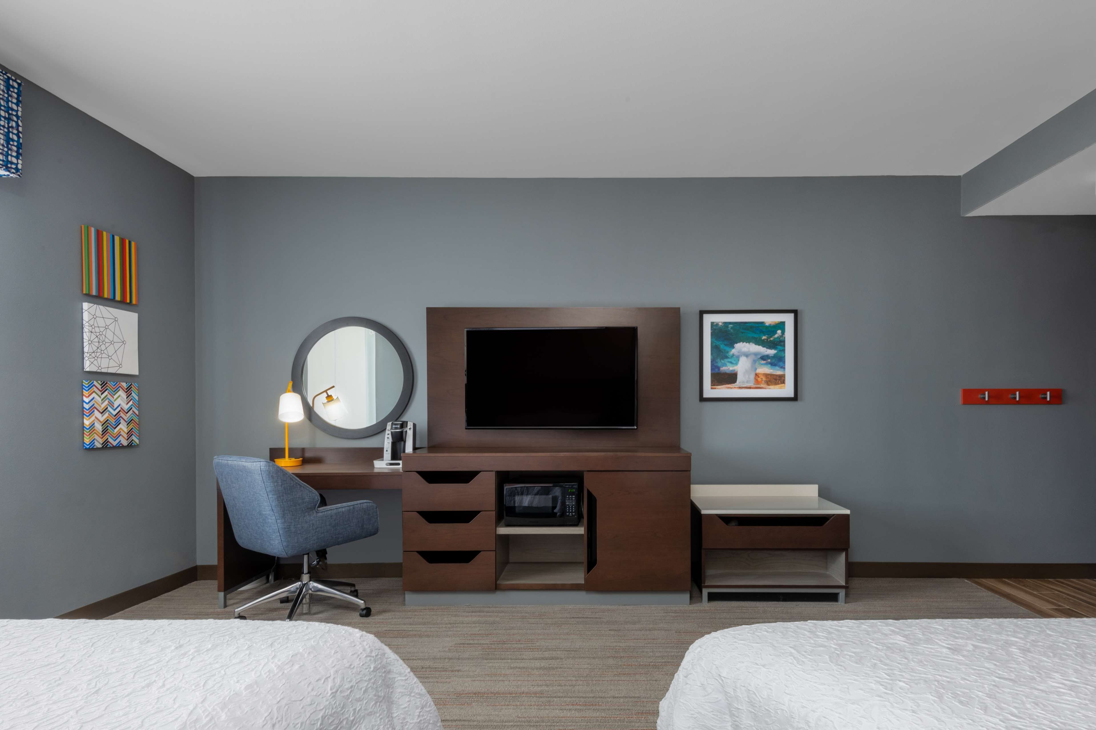 A hotel room with a bed, a desk with a chair, a TV, and artwork on the walls.