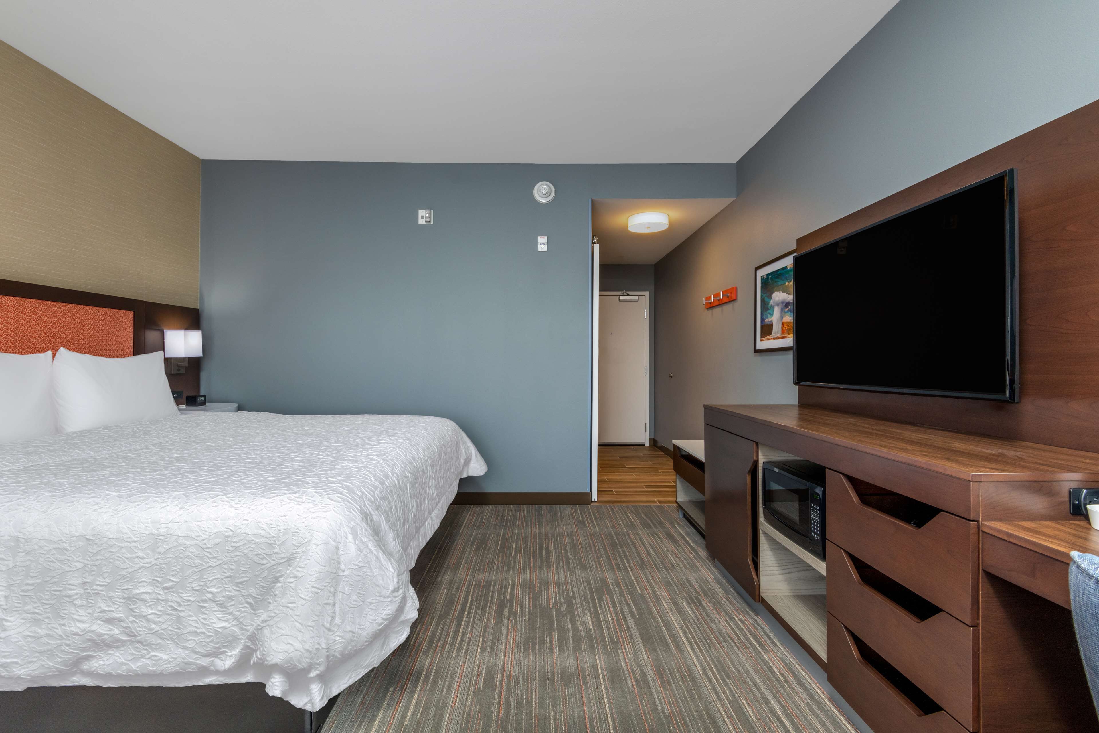 Habitación de hotel con cama, televisión de pantalla plana, escritorio con microondas y puerta que da a un baño.
