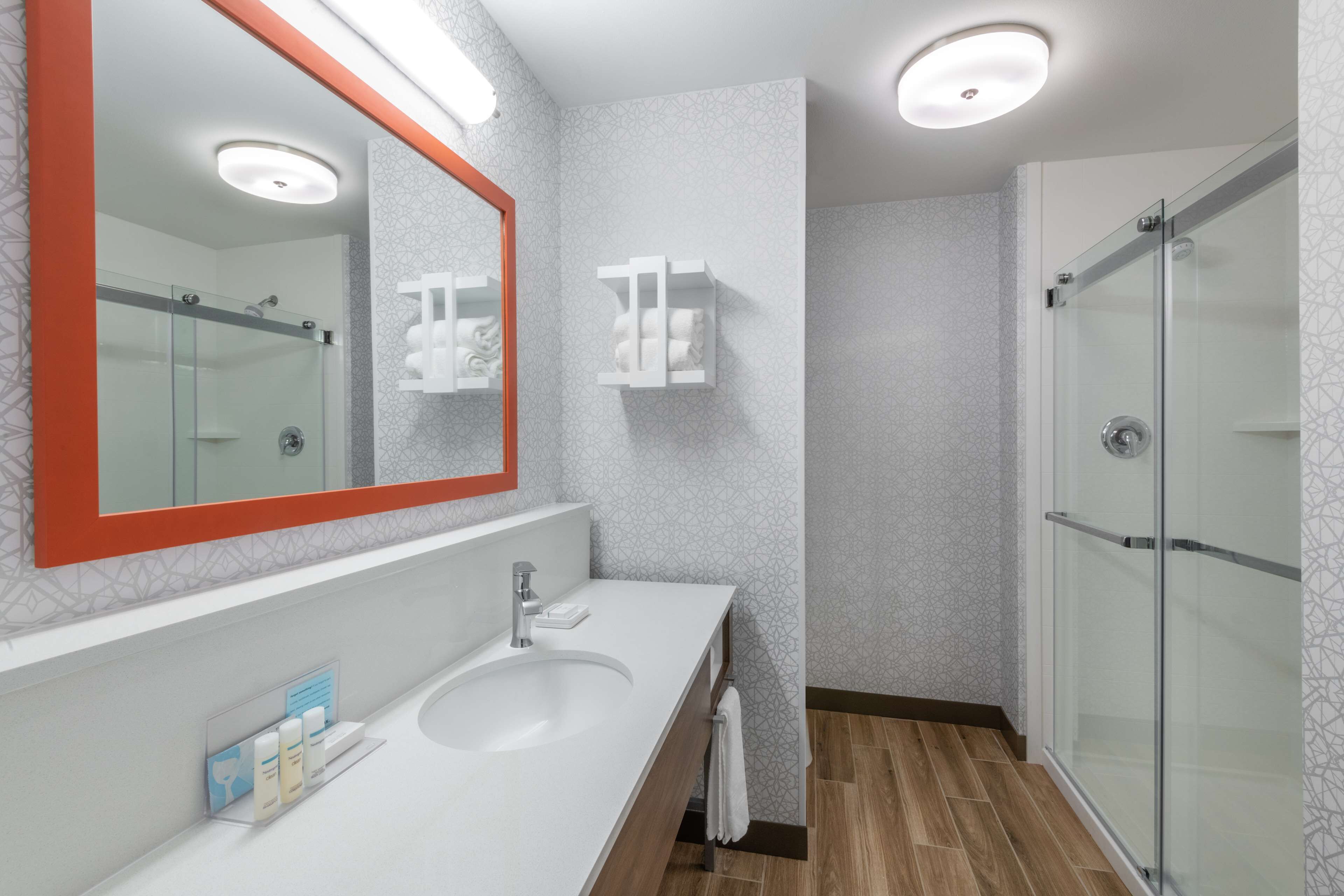 A modern bathroom with a large mirror, a white sink, and a glass shower enclosure.