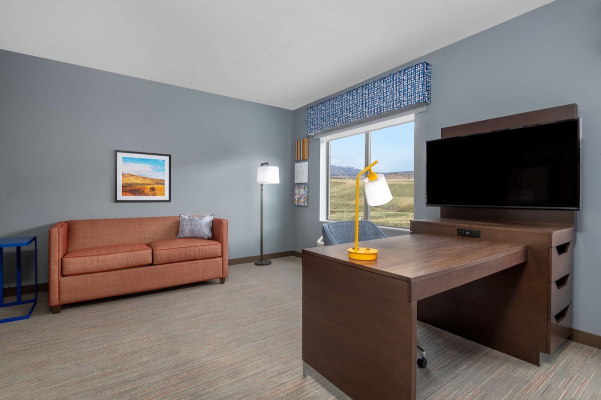 A modern living room with a sofa, a desk, a television, and a window with a view.
