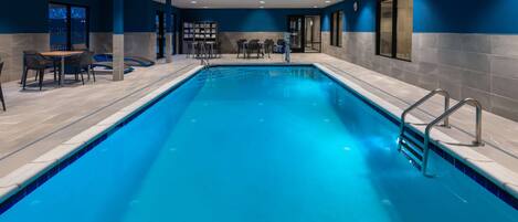 A swimming pool with a tiled deck, a seating area with tables and chairs, and a blue wall.
